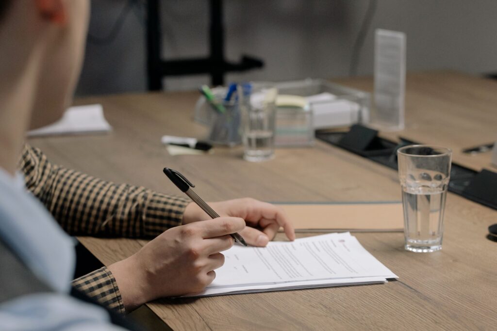 Pessoa assinando um contrato sobre a mesa de reunião. Foto de cottonbro studio via Pexels.
