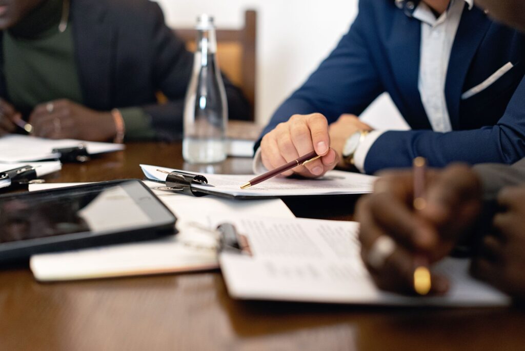 Mãos apontando para um contrato sobre a mesa durante reunião comercial. Foto de Mikhail Nilov via Pexels.