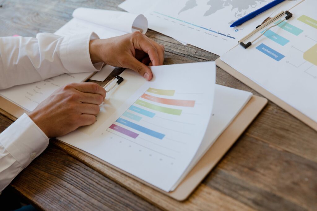 Mãos revisando um relatório mensal de marketing com gráficos sobre a mesa. Foto de RDNE Stock project via Pexels.